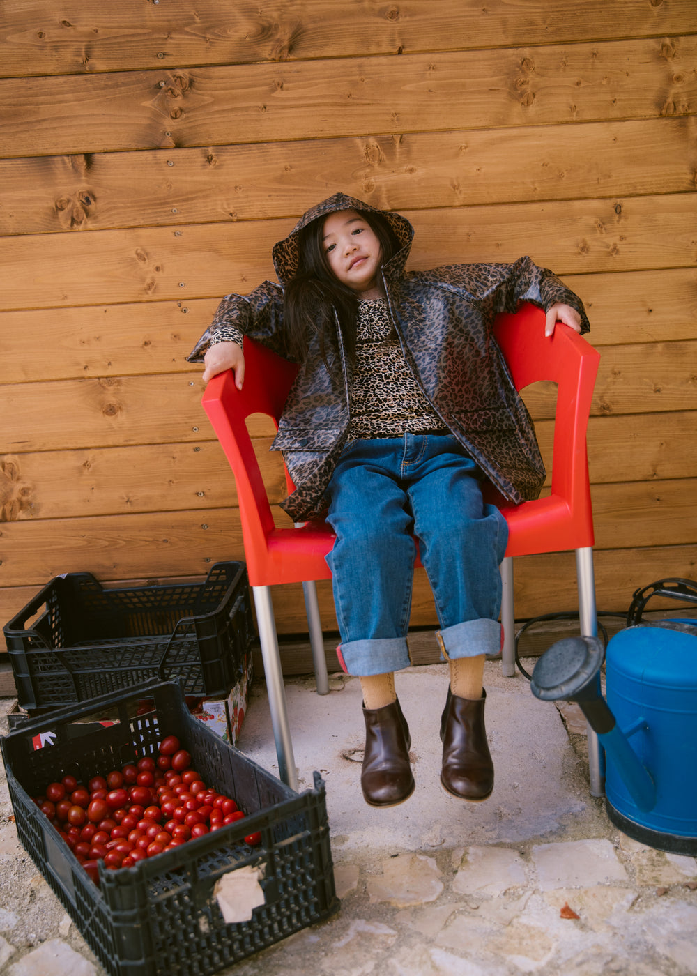 Barn sidder på en rød stol iført leopardmønstret regnjakke og jeans