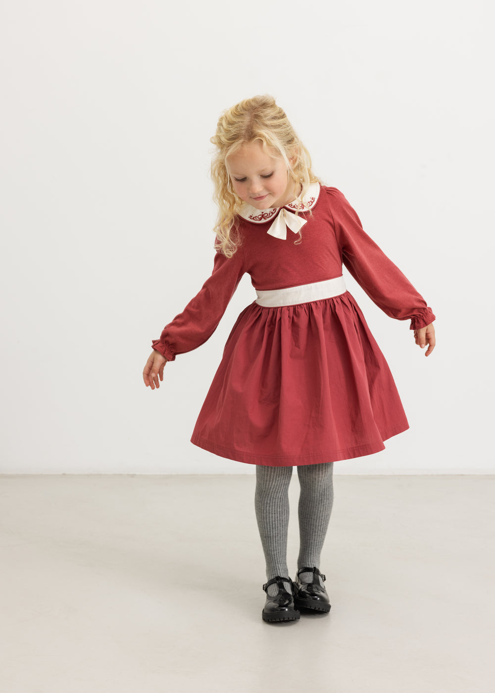 Burgundy dress with white collar and bow tie, gathered skirt and long sleeves.