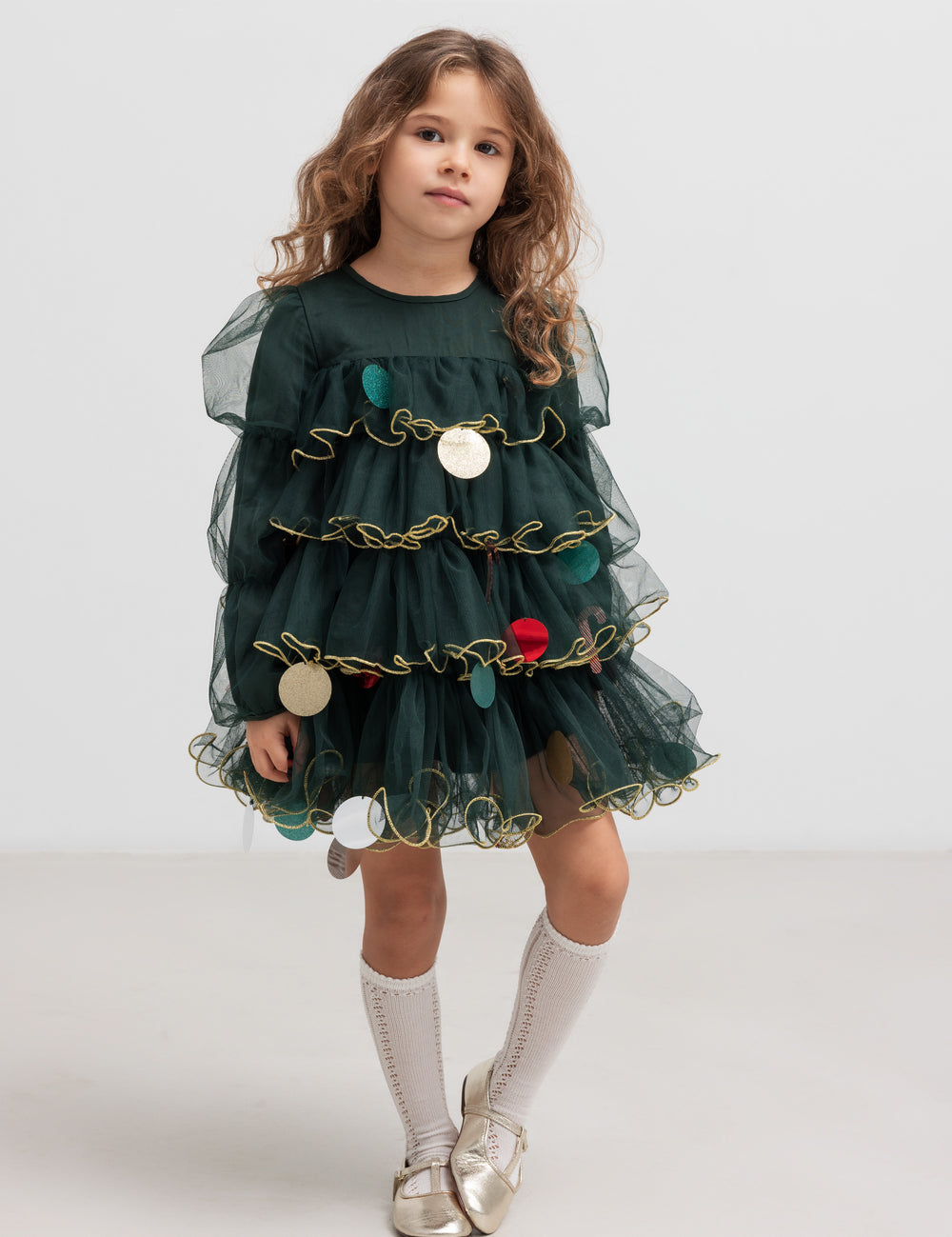 Pige iført mørkegrøn julekjole i tyl med guldkanter og juledetaljer til børn