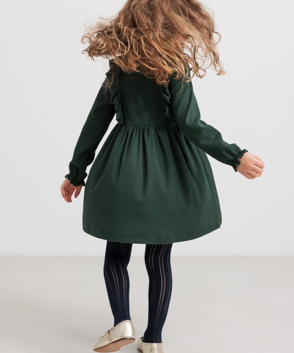 Pige iført grøn ribstrikket julekjole med flæser på skuldrene