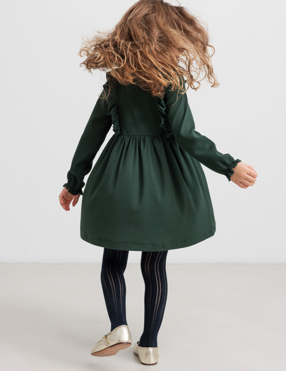 Pige iført grøn ribstrikket julekjole med flæser på skuldrene