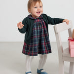 Baby iført mørkeblå grøn og rød ternet julekjole med hvide strømpebukser og grøn cardigan