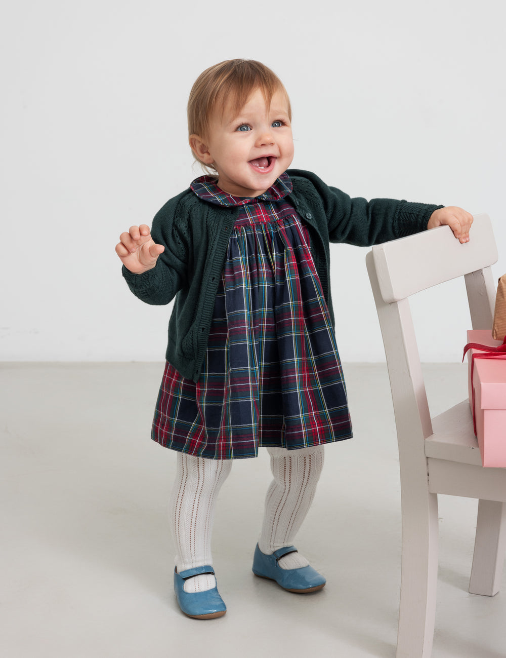 Baby wearing dark green cardigan with lace pattern and checkered red and green Christmas dress