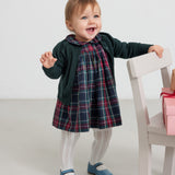 Lille pige iført cremefarvede ribstrikkede strømpebukser og ternet julekjole