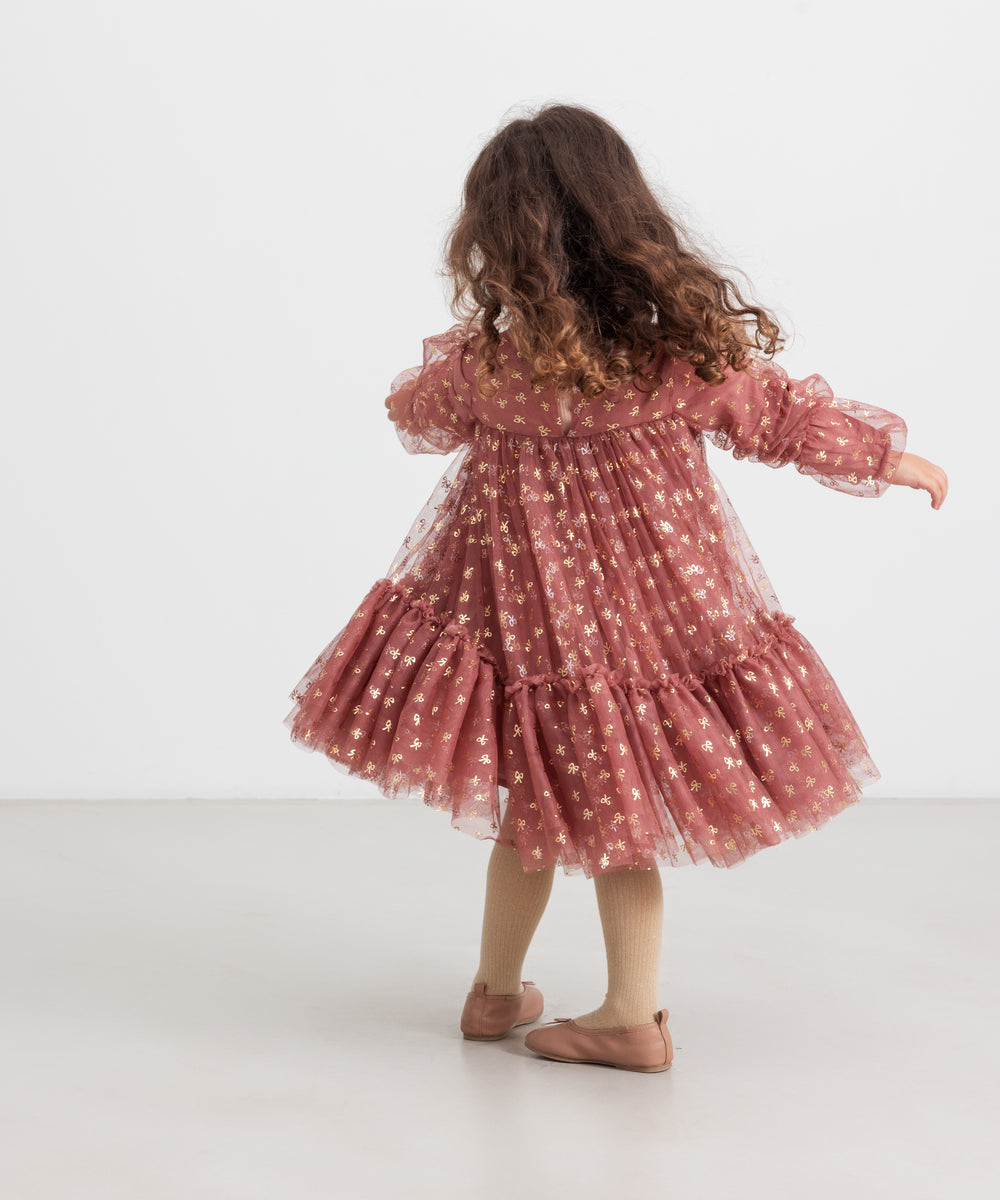 Pige iført rosa festkjole i tyl med guldprint og flæser til børn