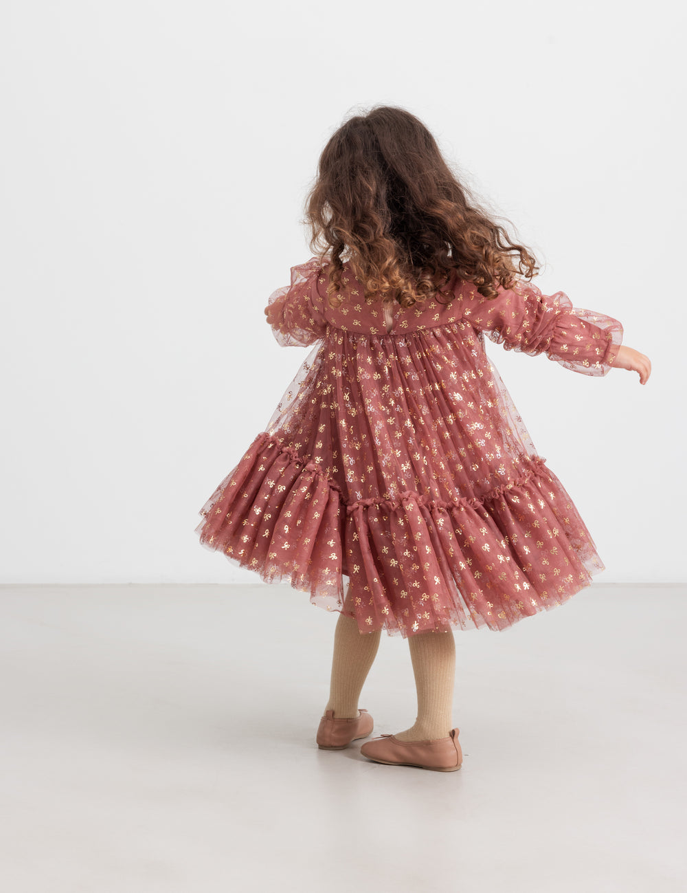 Pige iført rosa festkjole i tyl med guldprint og flæser til børn