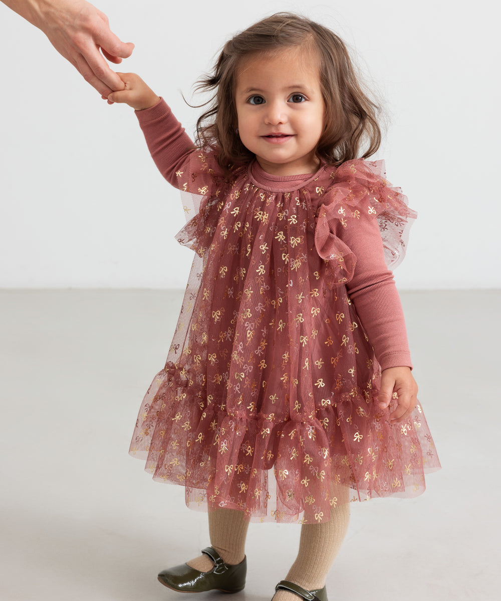 Baby iført rosa festlig kjole i tyl med flæser og gyldne detaljer