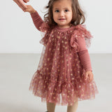 Baby iført rosa festlig kjole i tyl med flæser og gyldne detaljer