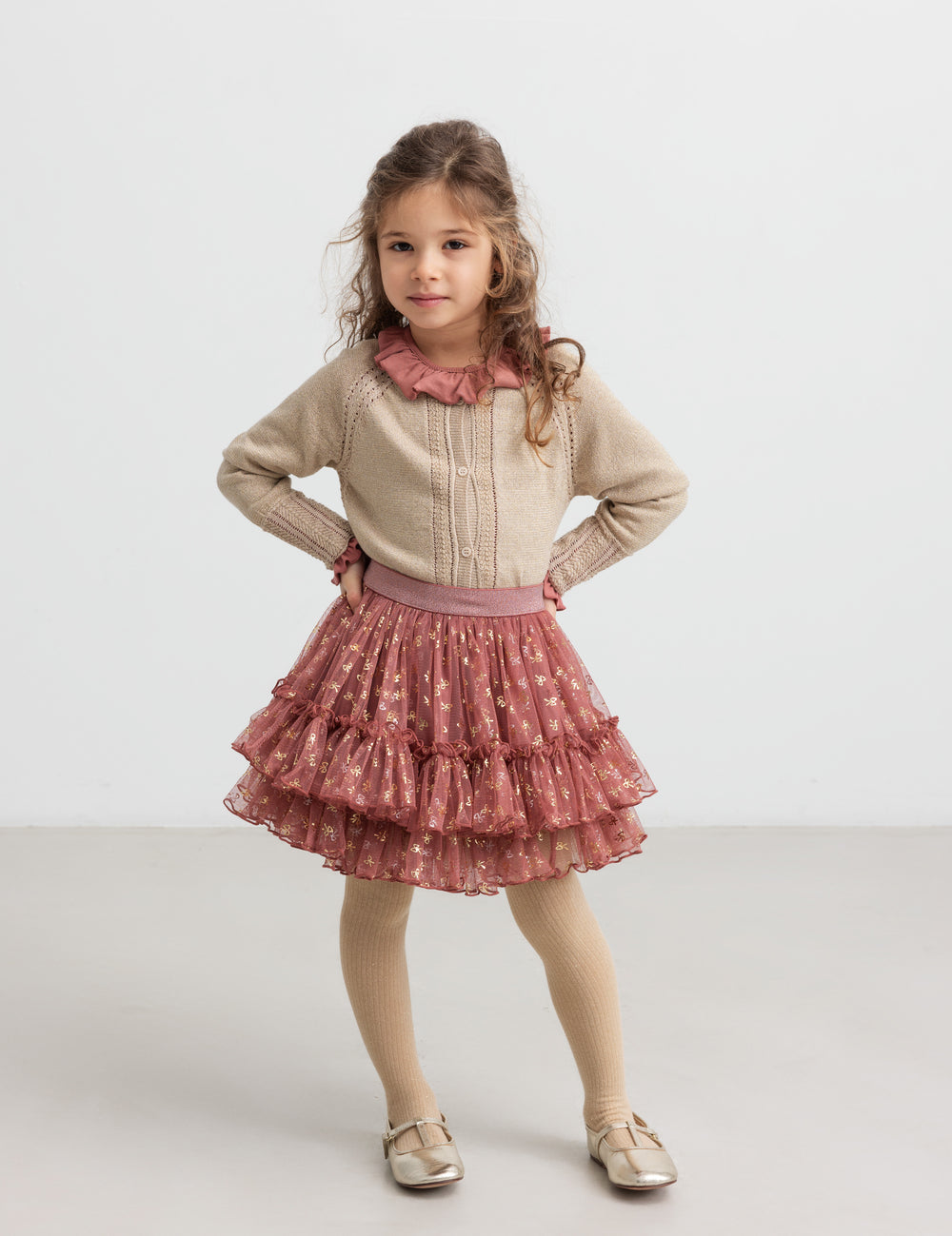 Girl wearing beige cardigan with gold glitter, pink party skirt and children's tights