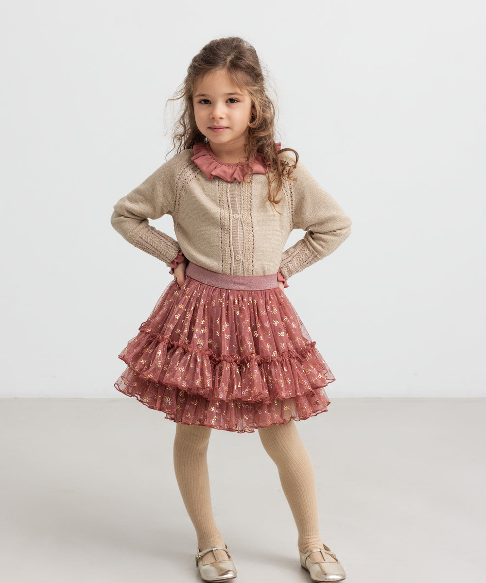 Pige iført støvet rosa bluse, glimmercardigan og lyserød festnederdel i tyl