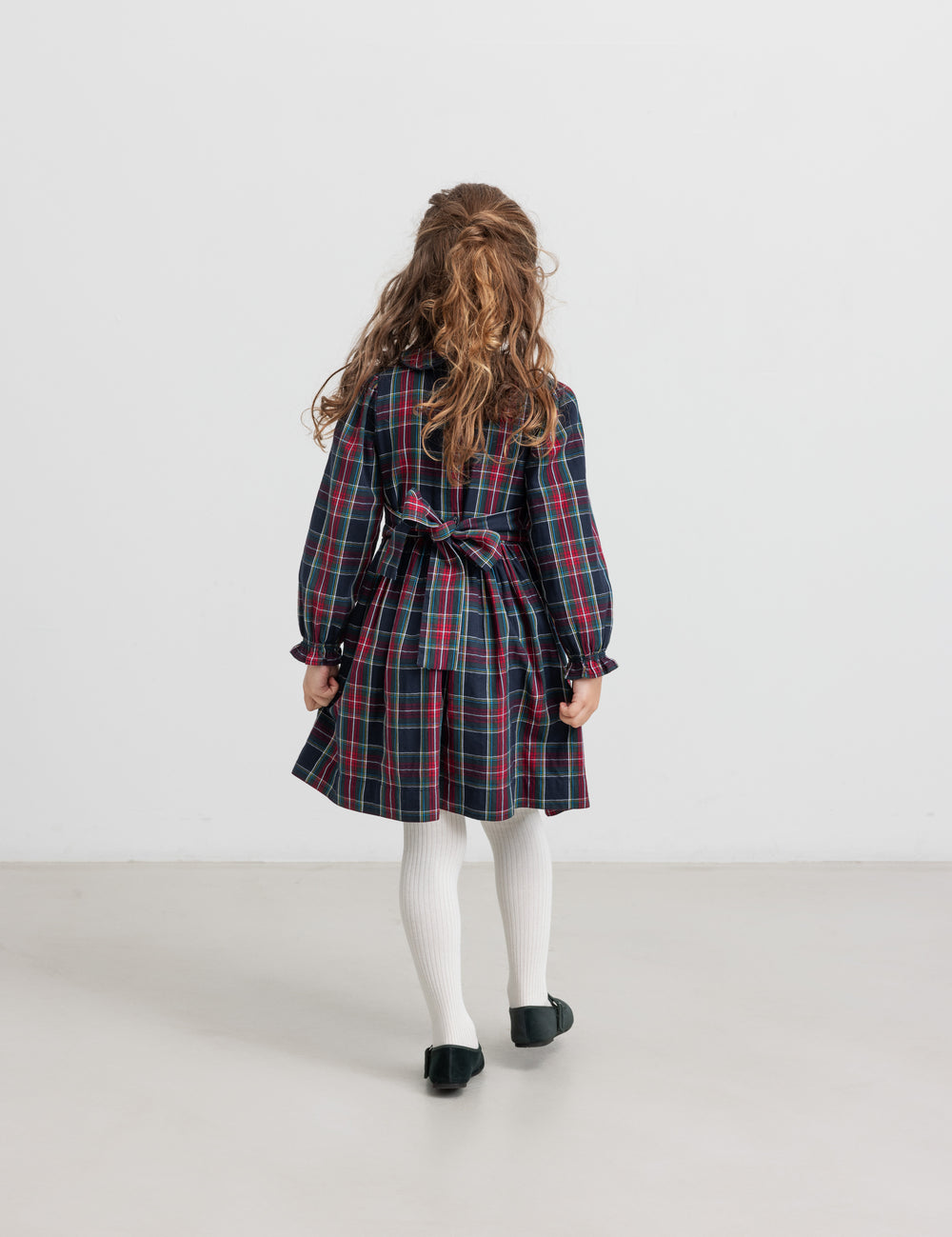 Pige iført mørkeblå og rød ternet julekjole med krave og hvide strømpebukser til børn