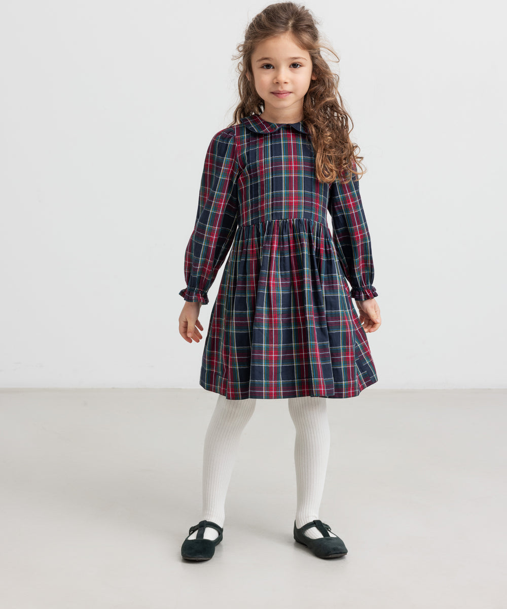 Pige iført mørkeblå og rød ternet julekjole med krave og hvide strømpebukser til børn