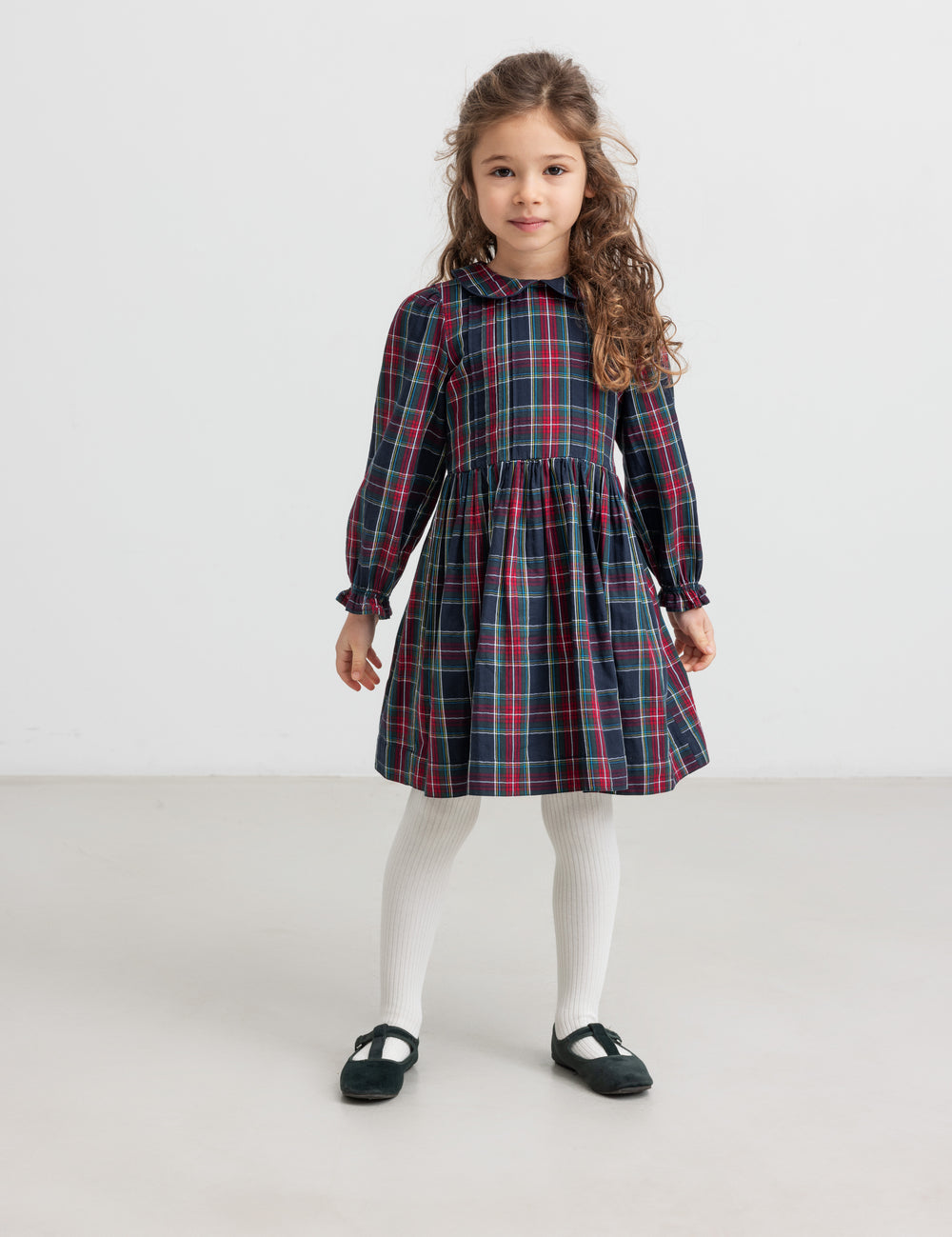 Pige iført mørkeblå og rød ternet julekjole med krave og hvide strømpebukser til børn