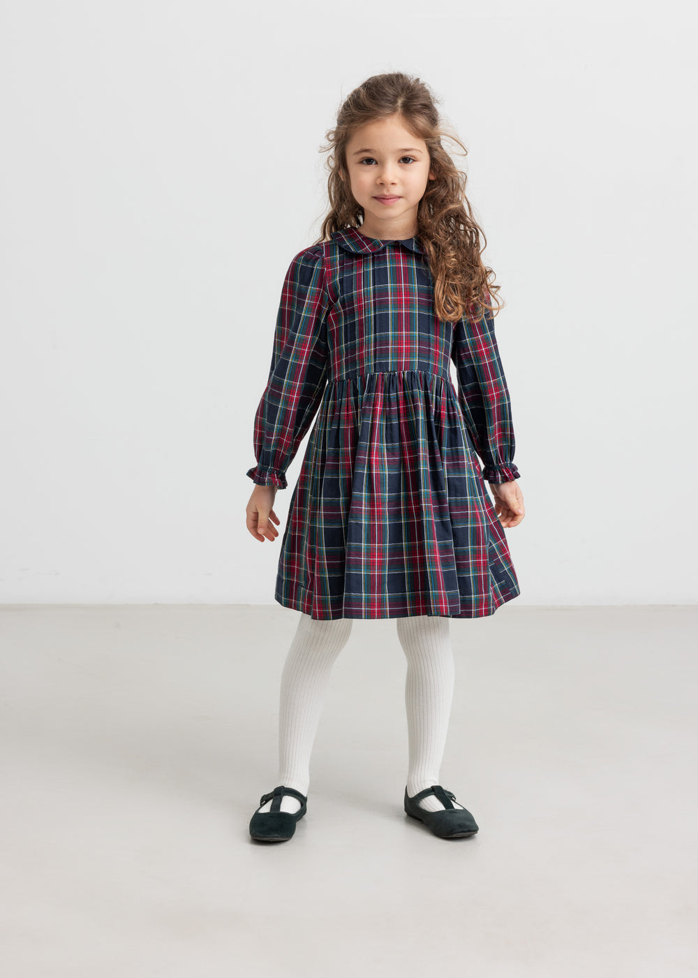 Pige iført ternet julekjole og cremefarvede strømpebukser til børn