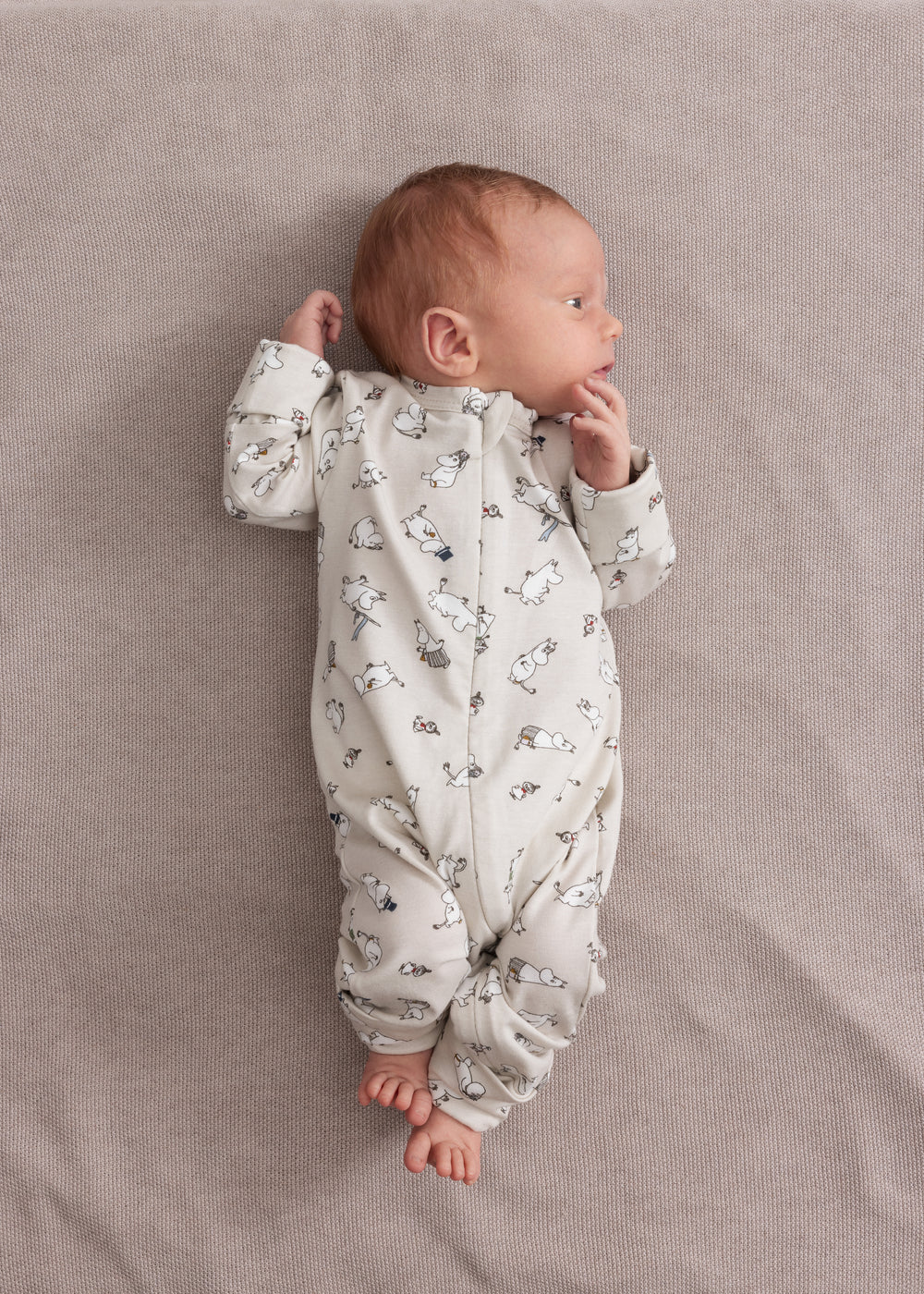 Baby iført lys heldragt med Moomin-mønster