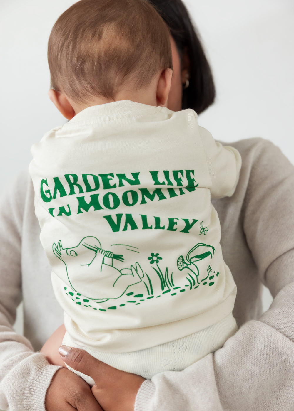 Baby wearing a white t-shirt with a green Moomin print.