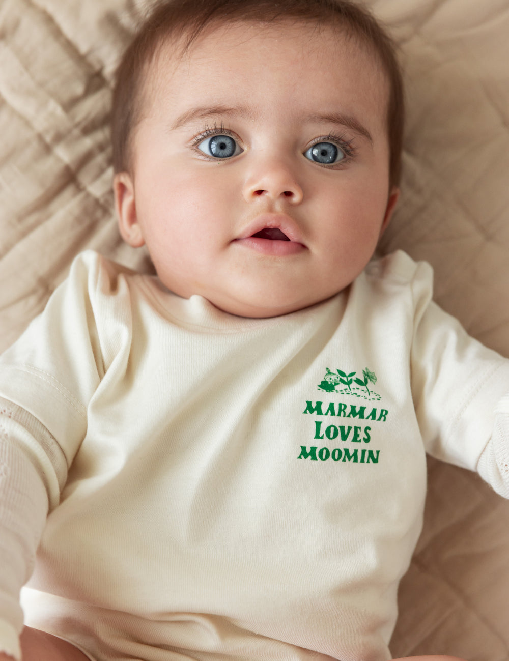 Baby wearing a white t-shirt with a green Moomin print.