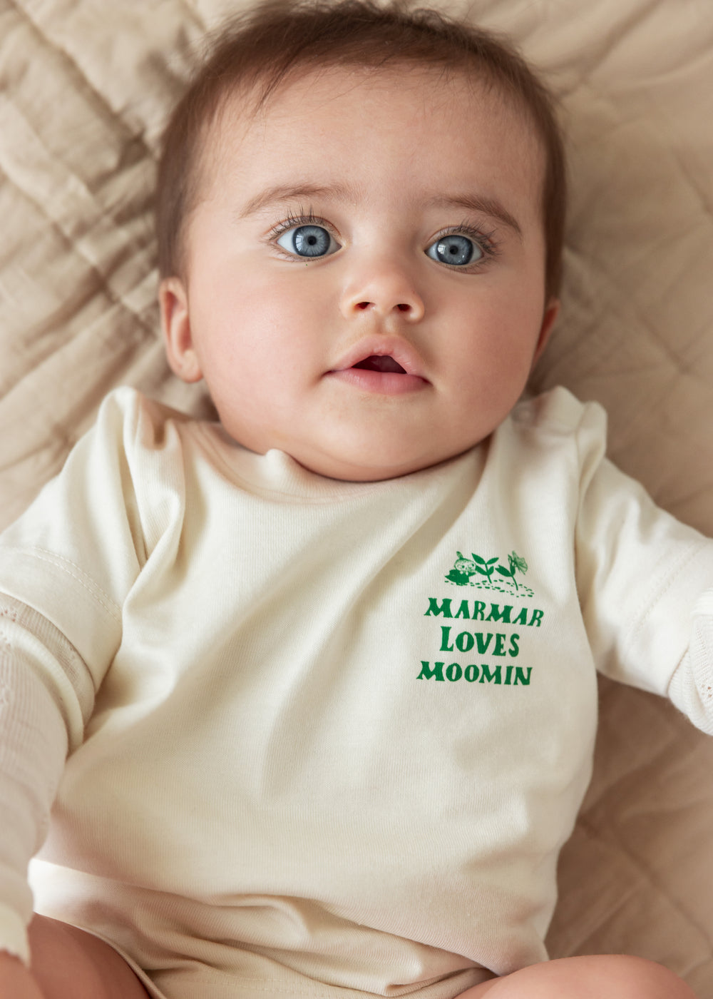 Baby wearing a white t-shirt with a green Moomin print.