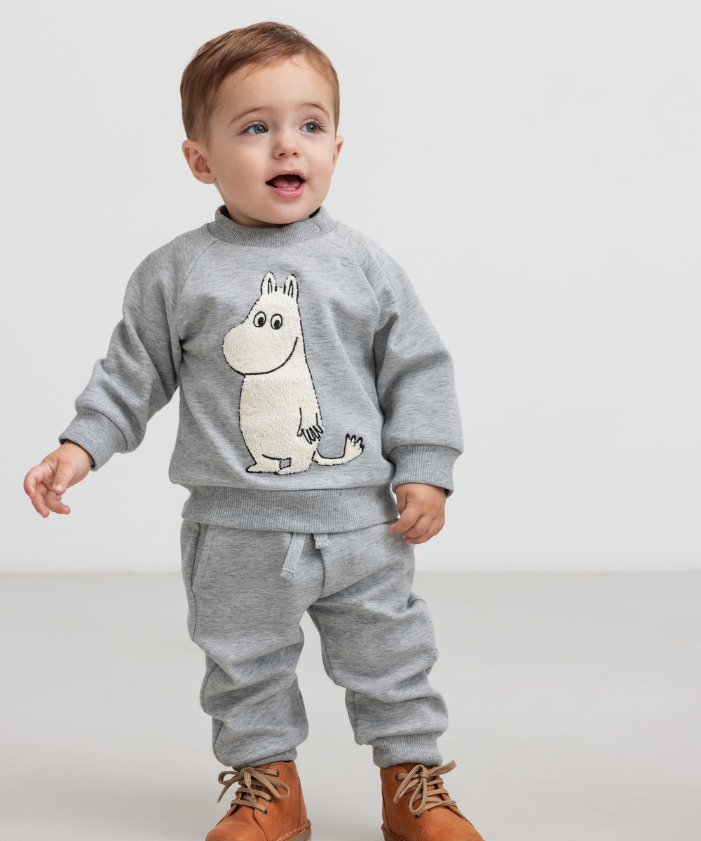 Lille børn iført grå sweatshirt med Moomin print og grå joggingbukser