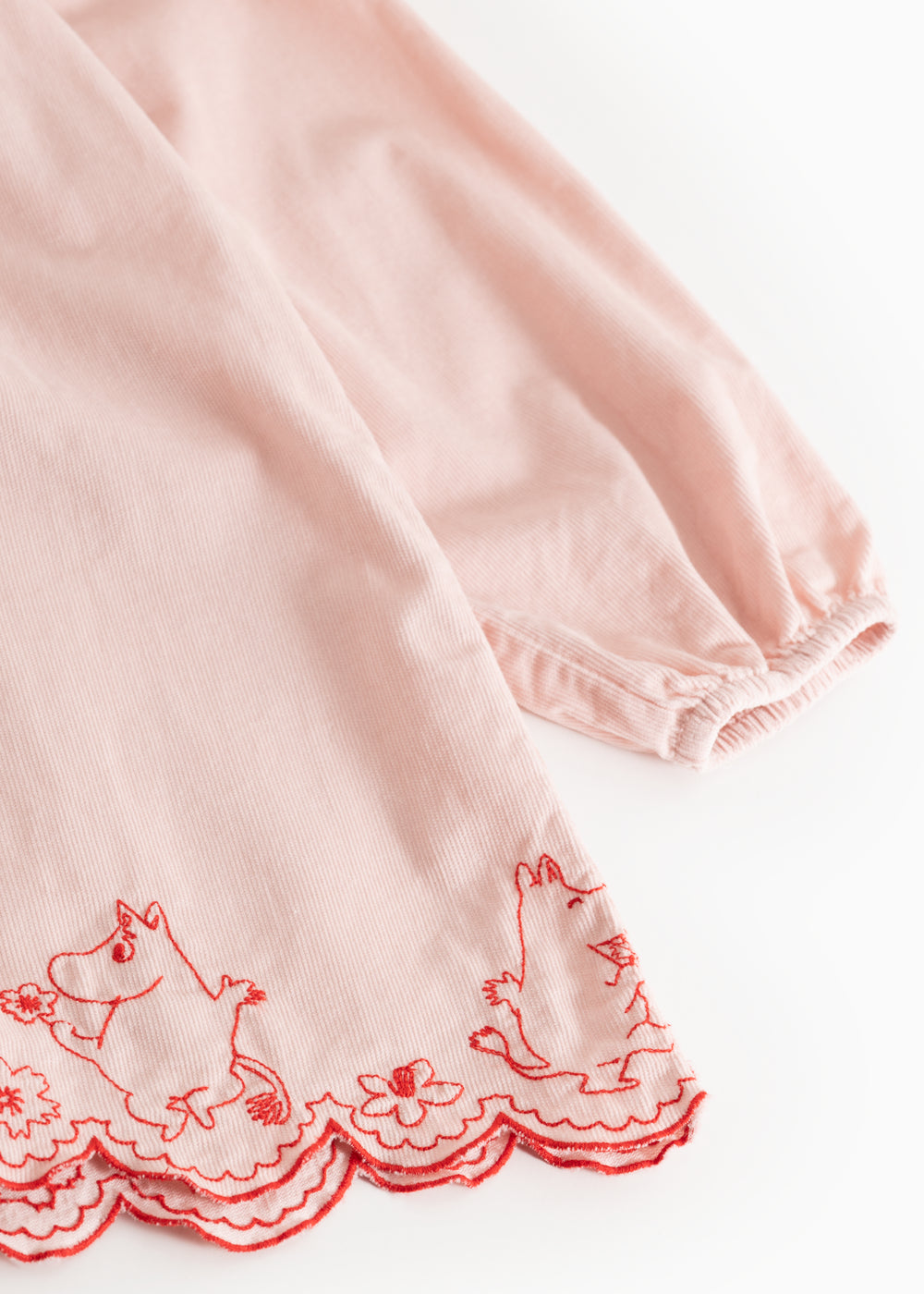 Pink dress with red embroidered pattern edge and wavy bottom edge.