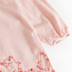 Pink dress with red embroidered pattern edge and wavy bottom edge.