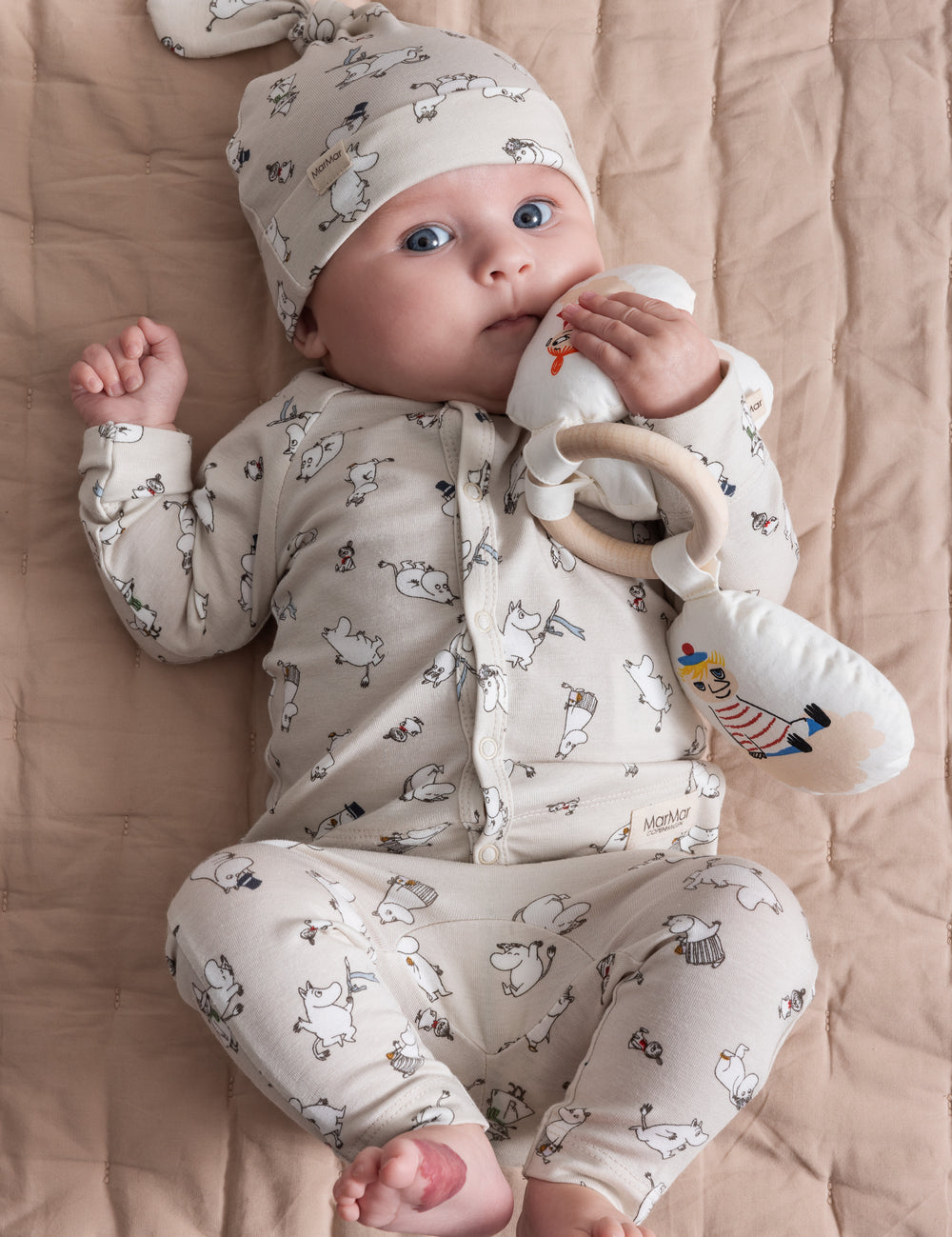 Baby iført lyst Moomin-print bukser og en hue.