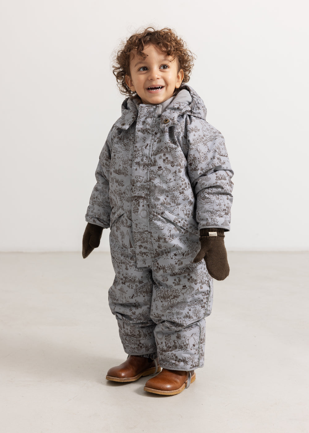 Child in a gray winter suit with dark brown knitted gloves and brown boots
