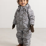 Child in a gray winter suit with dark brown knitted gloves and brown boots