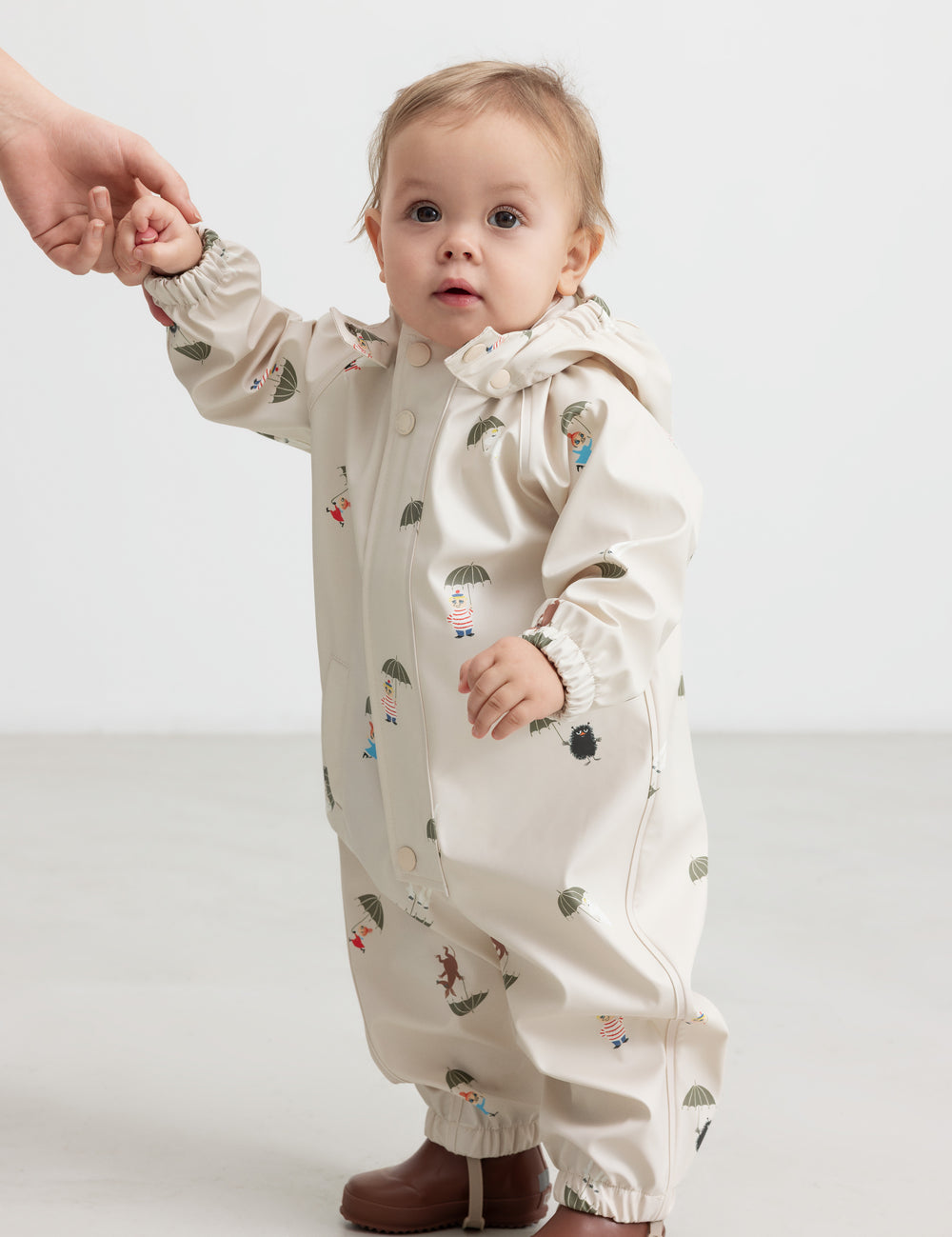Baby wearing a beige raincoat with Moomin print and hood.
