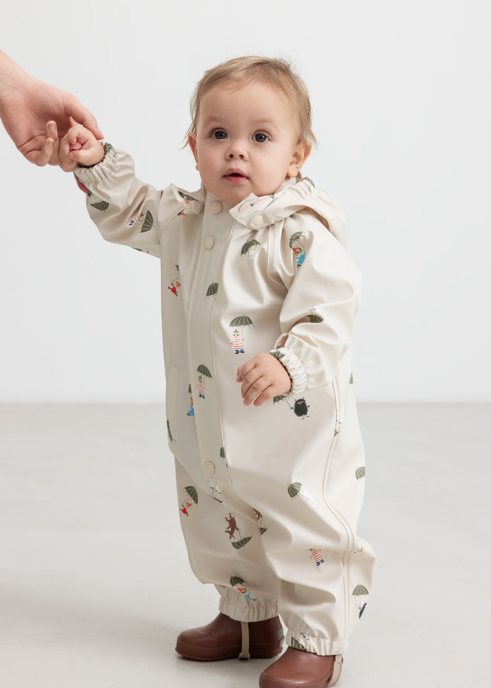 Baby wearing a beige raincoat with Moomin print and hood.