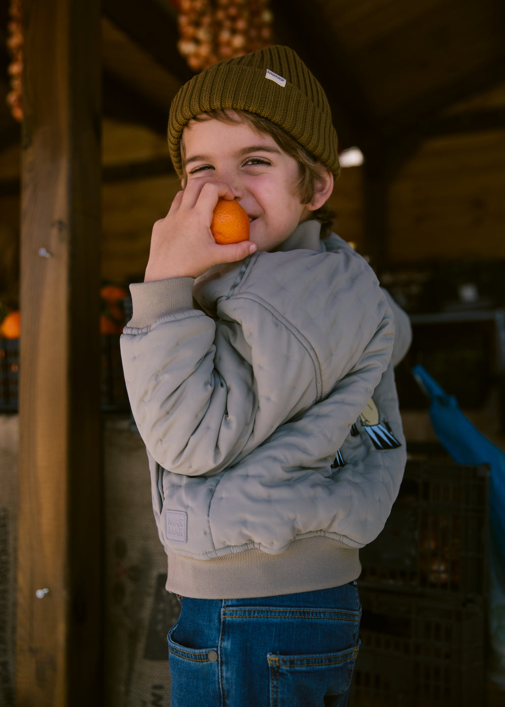 Children in green Moomin jackets holding fruit.