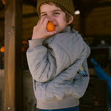 Children in green Moomin jackets holding fruit.