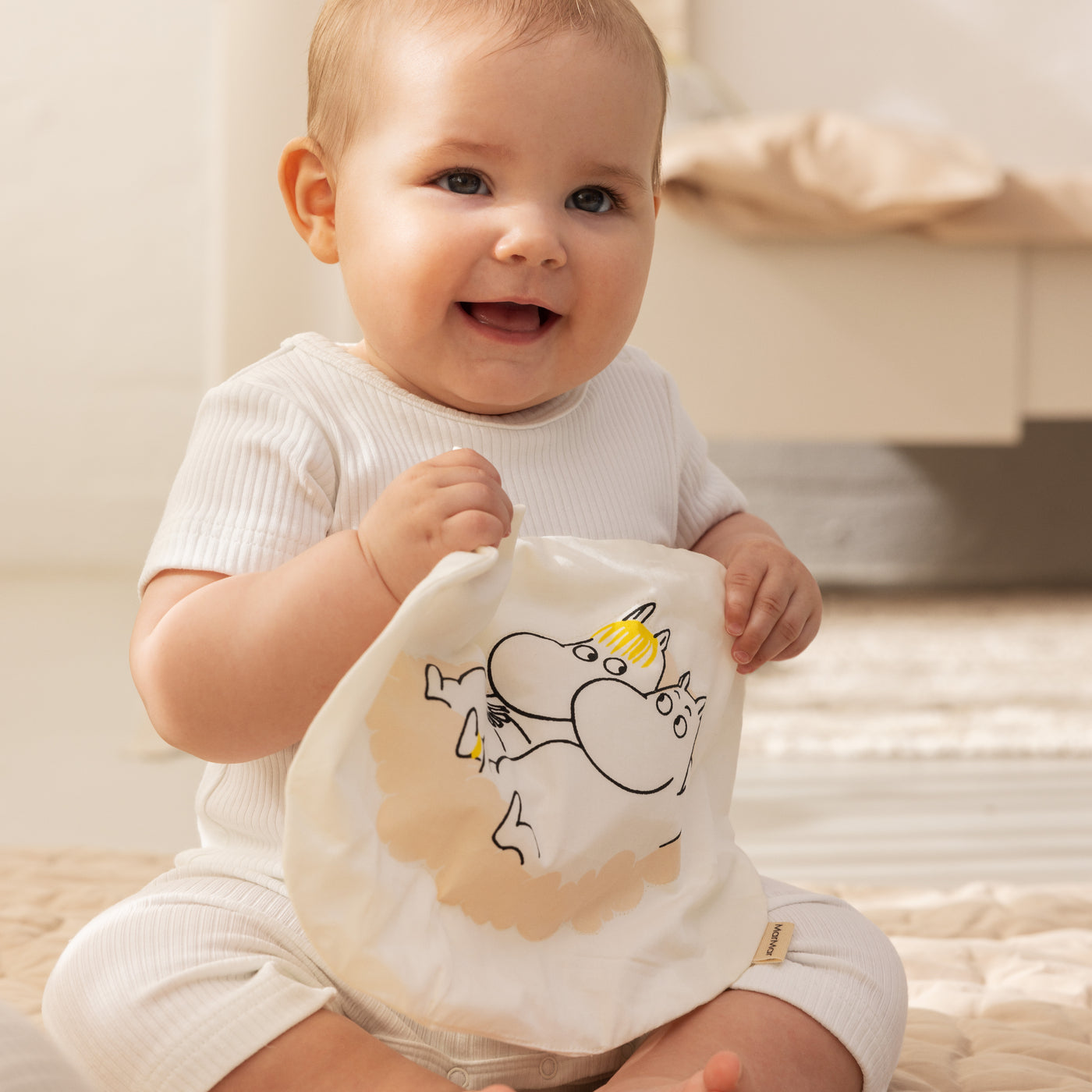 Baby sidder og holder en legetøj med Moomin motiv