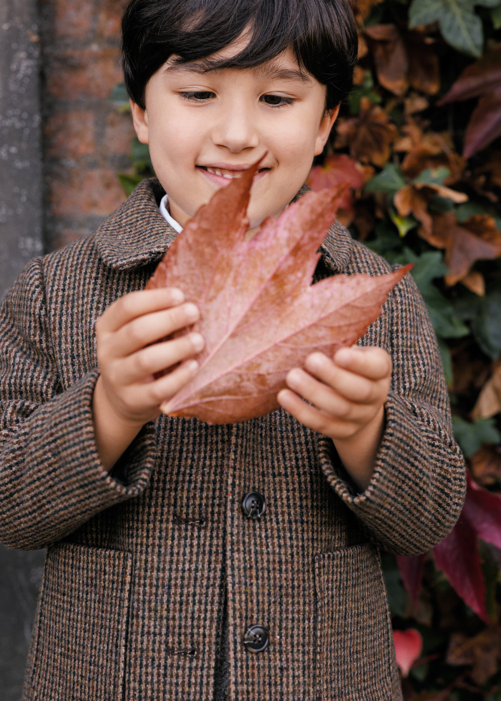 Dreng holder efterårsblad iført brun ternet jakke