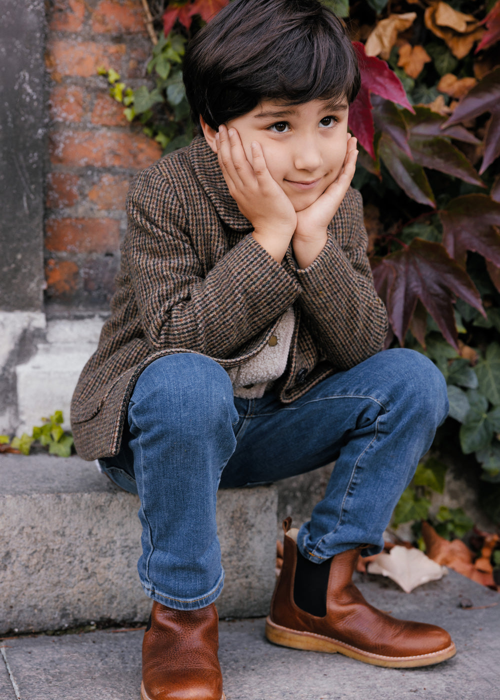 Barn i brun ternet jakke sidder på trappe