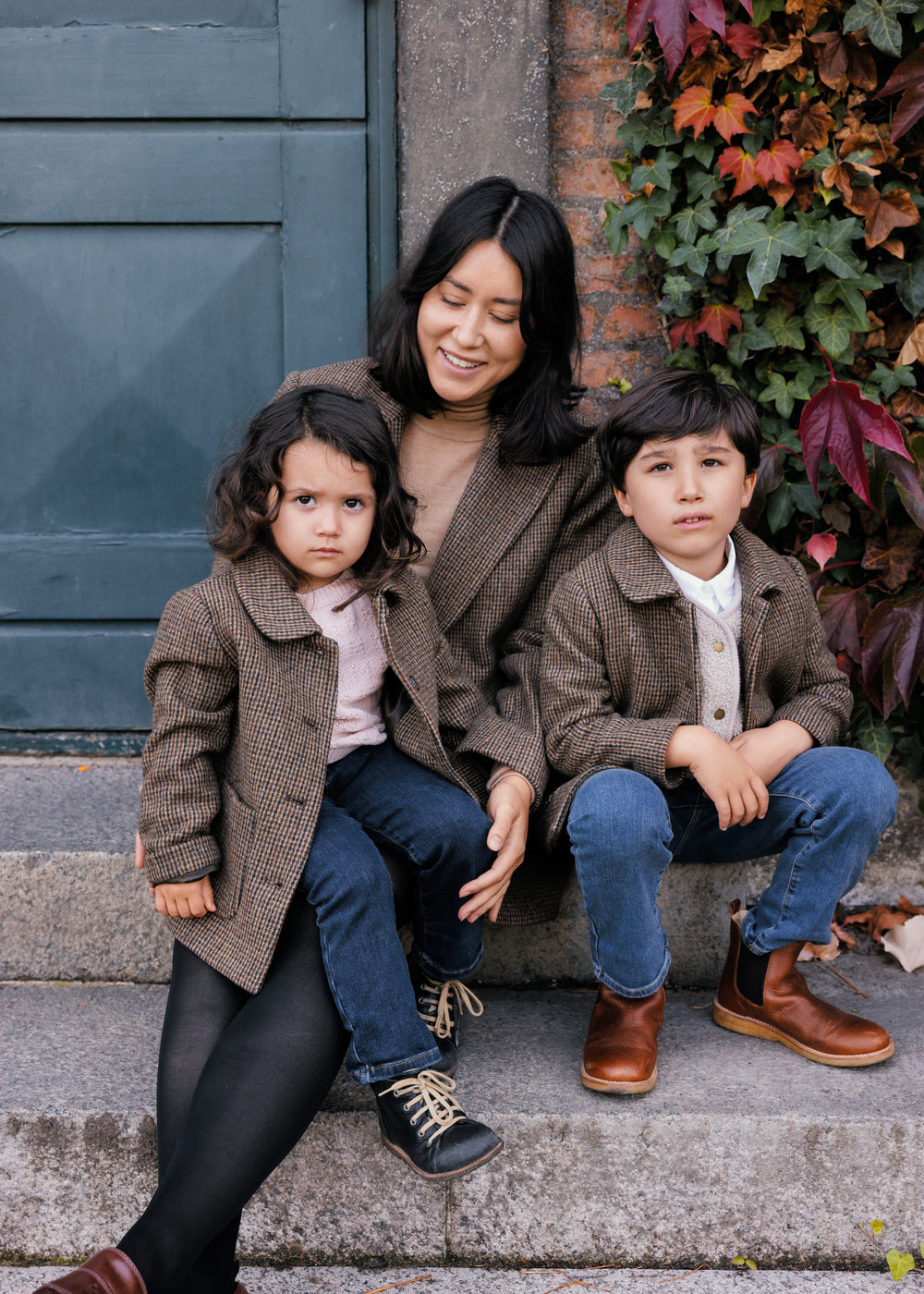 Mor og børn iført brune uldfrakker foran grøn dør