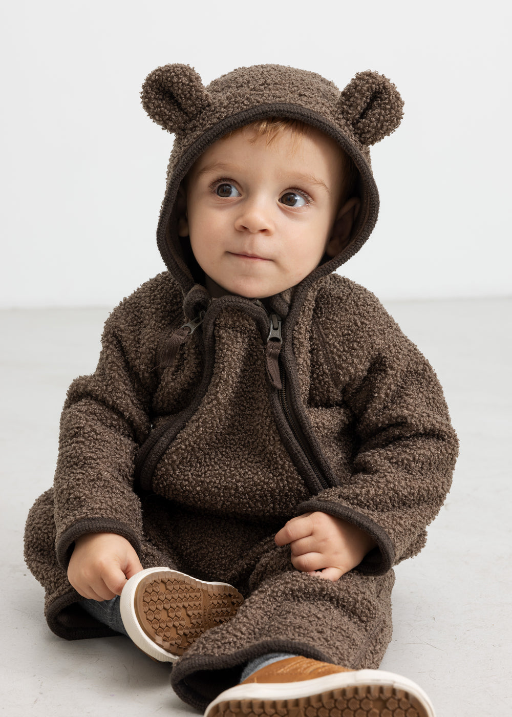 Baby i brun heldragt med ører, sidder og kigger op