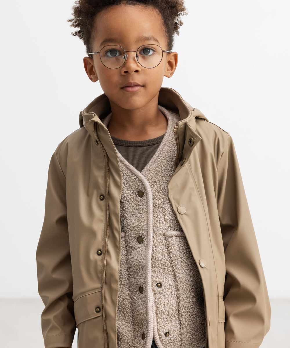 Barn iført beige regnjakke, hætten taget af og jakken åben