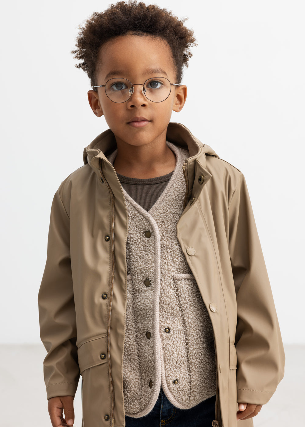 Barn iført beige regnjakke, hætten taget af og jakken åben