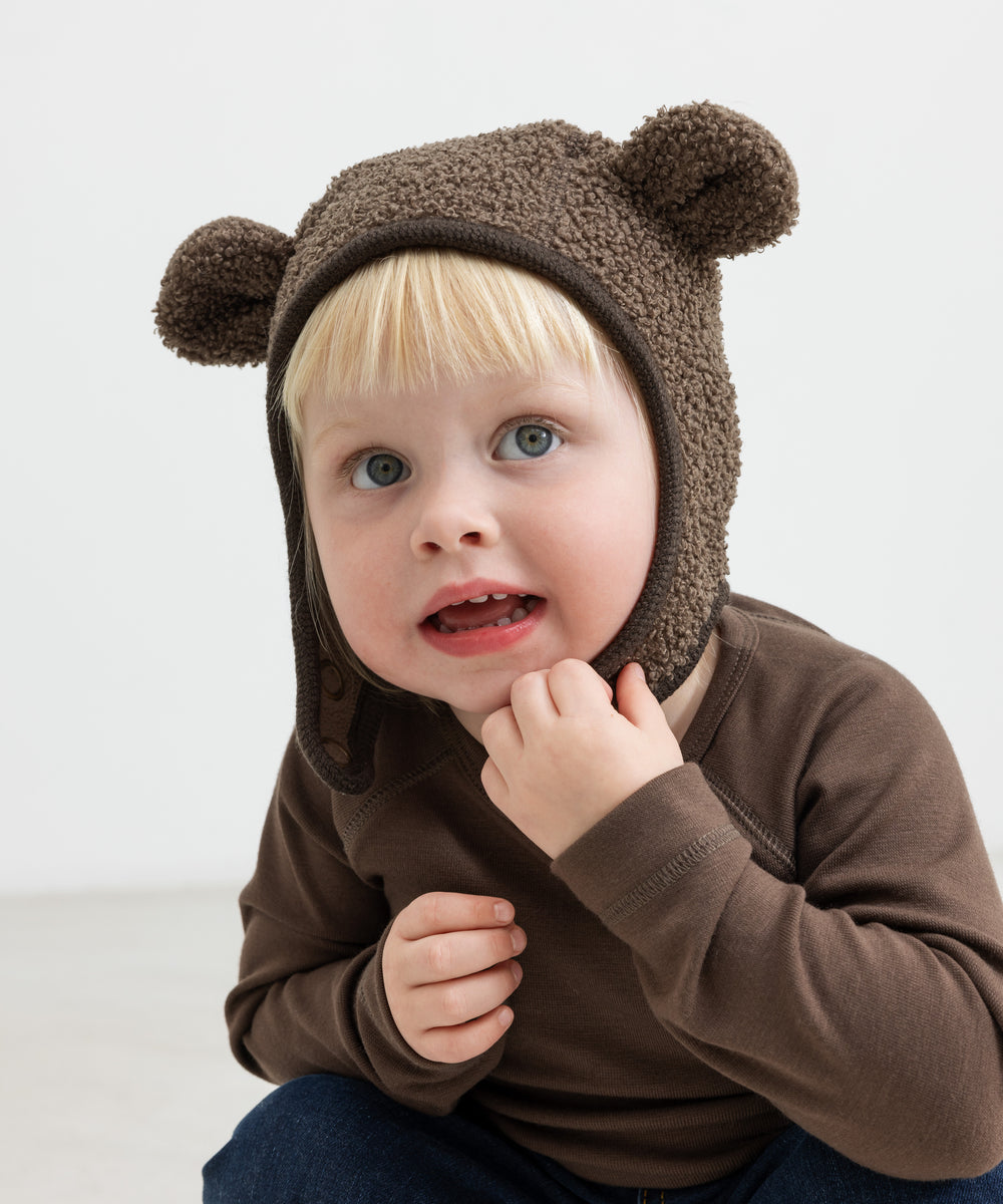 Barn iført brun elefanthue med ører i teddyfleece, sidder og kigger op