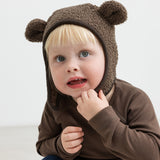 Barn iført brun elefanthue med ører i teddyfleece, sidder og kigger op