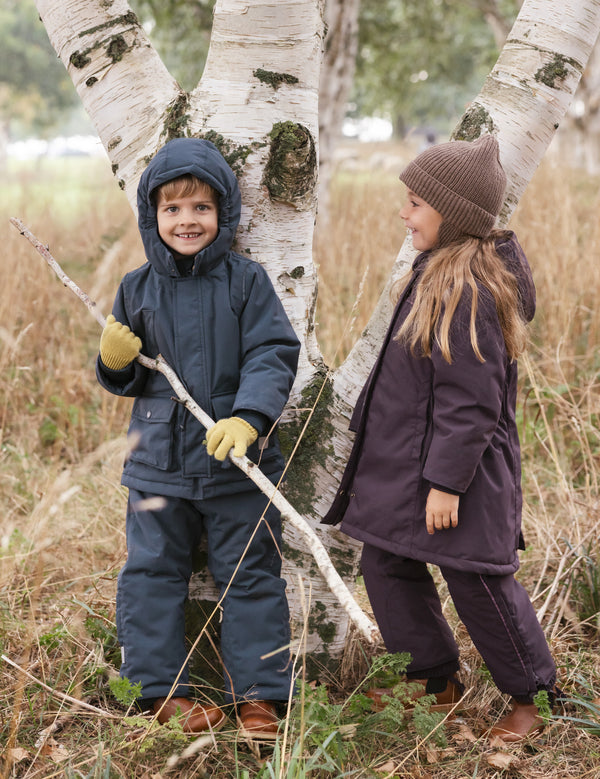 To børn iført vinterovertøj leger i naturen ved et birketræ