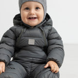 Smilende baby i mørkegrå dundragt sidder på gulv