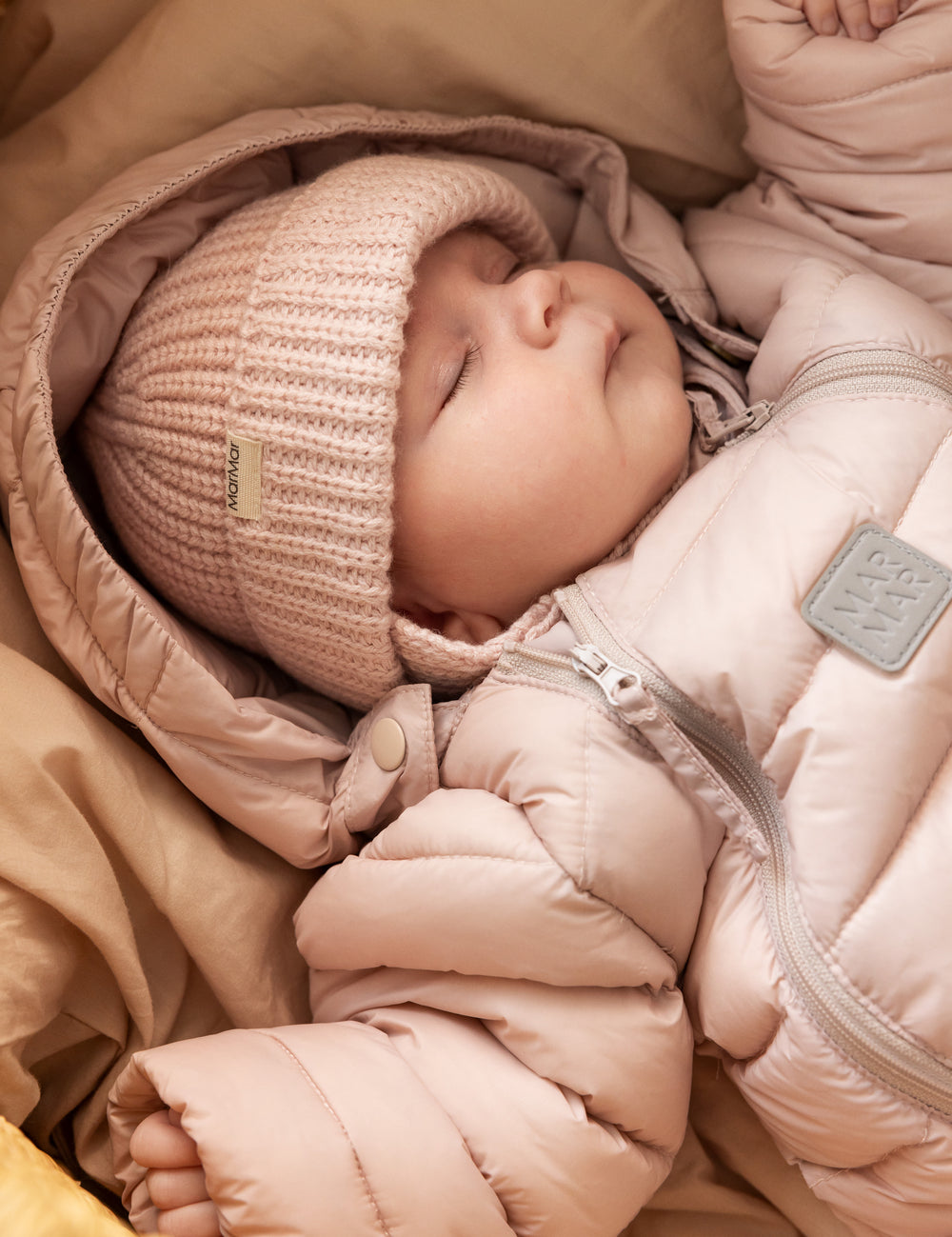 Baby iført lyserød dundragt og strikket hat