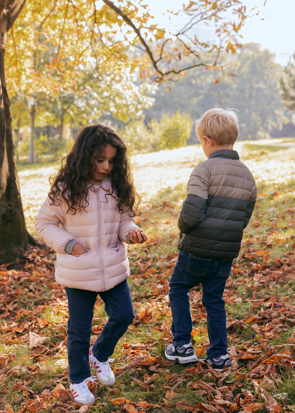 To børn iført vatterede jakker leger i efterårslandskab