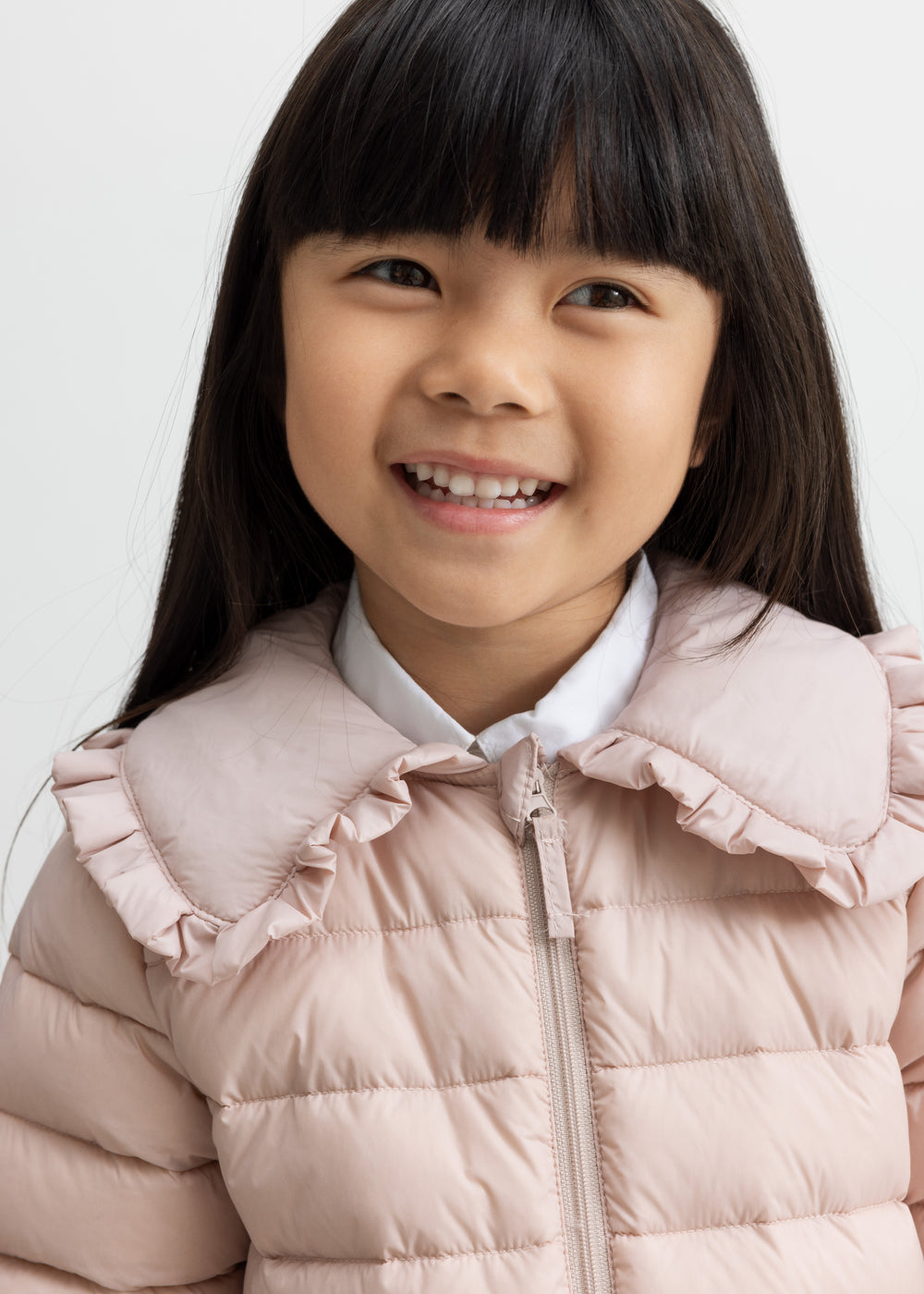 Barn i lyserød vatteret jakke med flæsekrave smiler