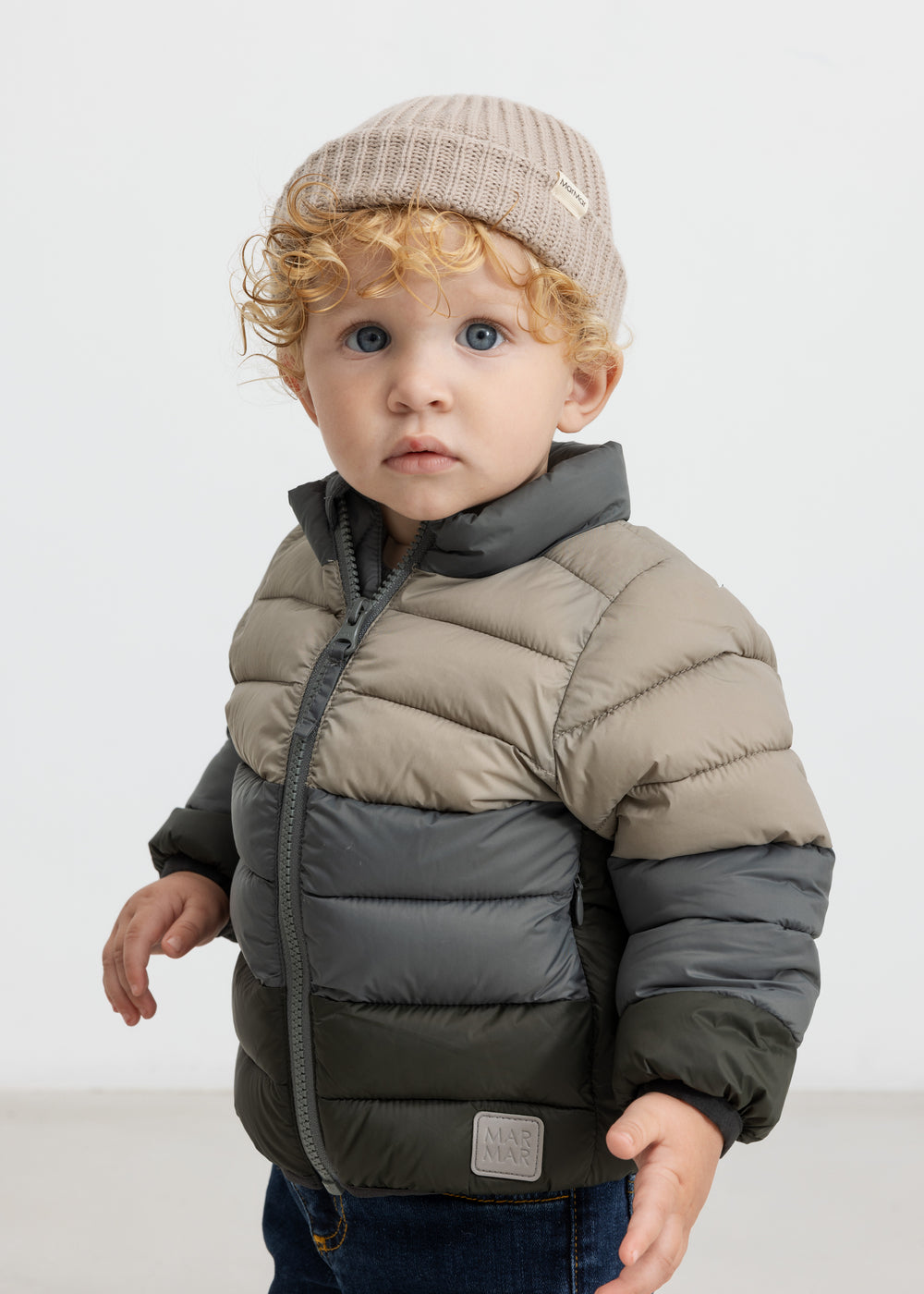 Dreng med beige hue iført vatteret jakke i grønne og beige toner