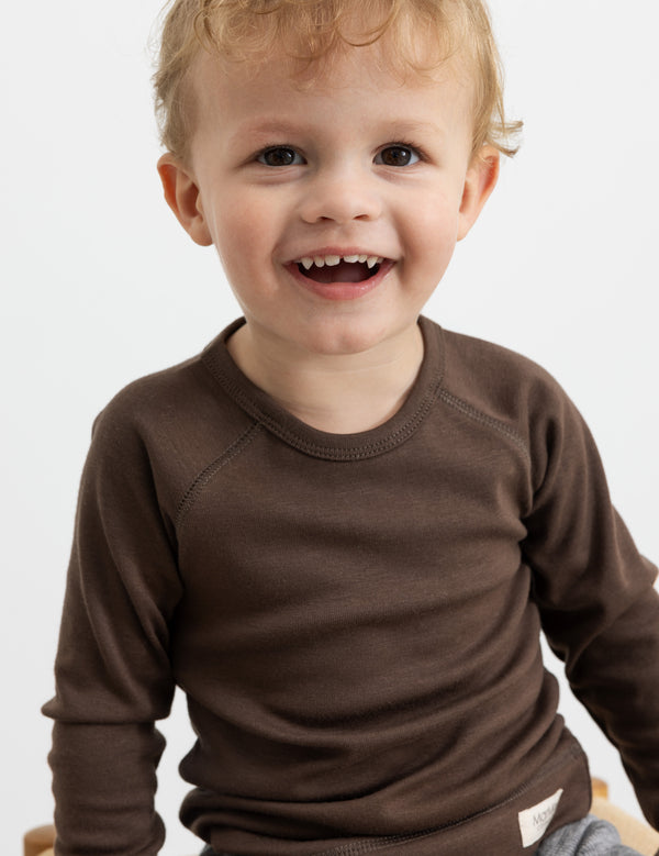 Smilende barn iført brun bluse med lange ærmer