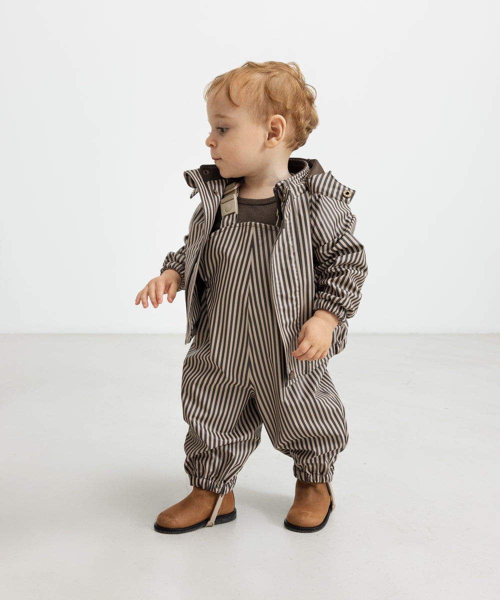 Baby i regnsæt med brune striber og hætte, står op