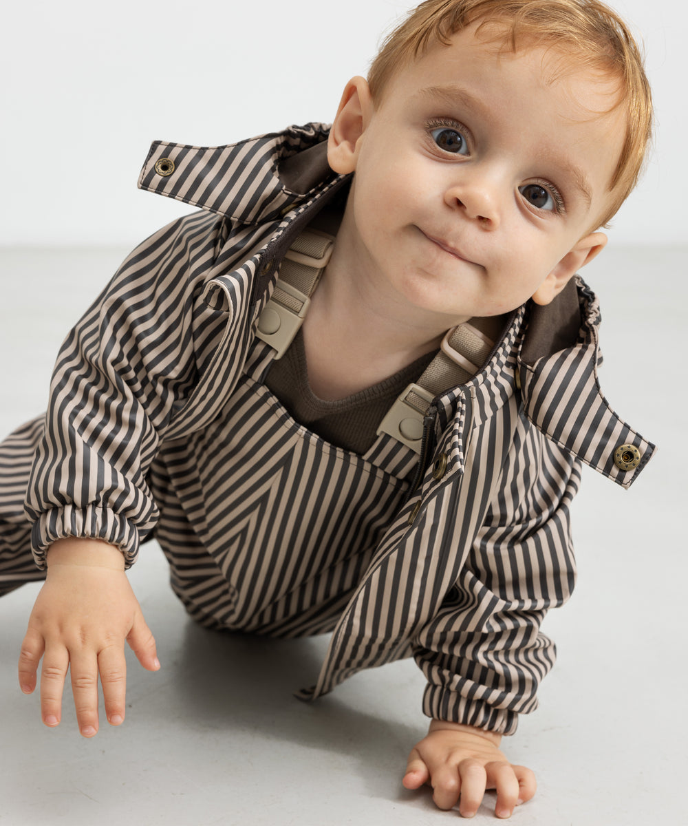 Baby i regnbukser med brune striber og jakke, kravler fremad